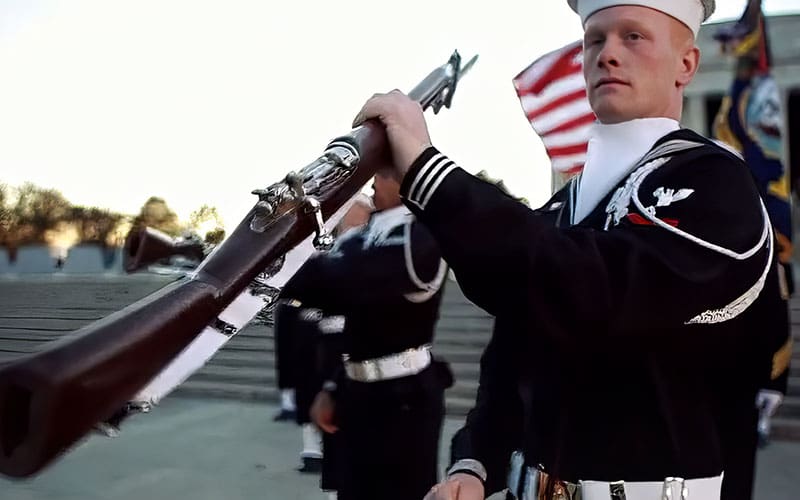 A man in navy uniform holding an old rifle.